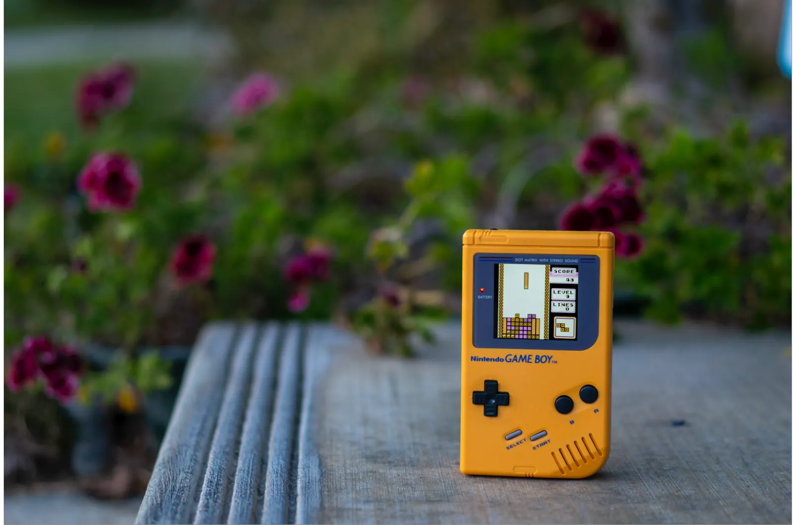 Yellow original Game Boy photographed outdoors on a wooden bench